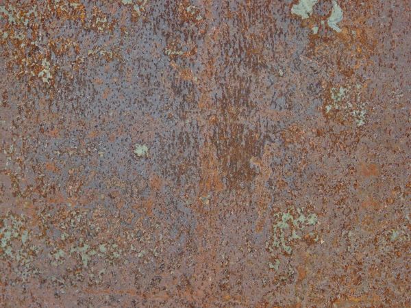 Rough blue rust texture, with various dark streaks and spots, covering a metal surface.